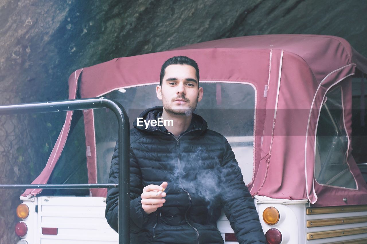 Portrait of young man exhaling smoke against vehicle