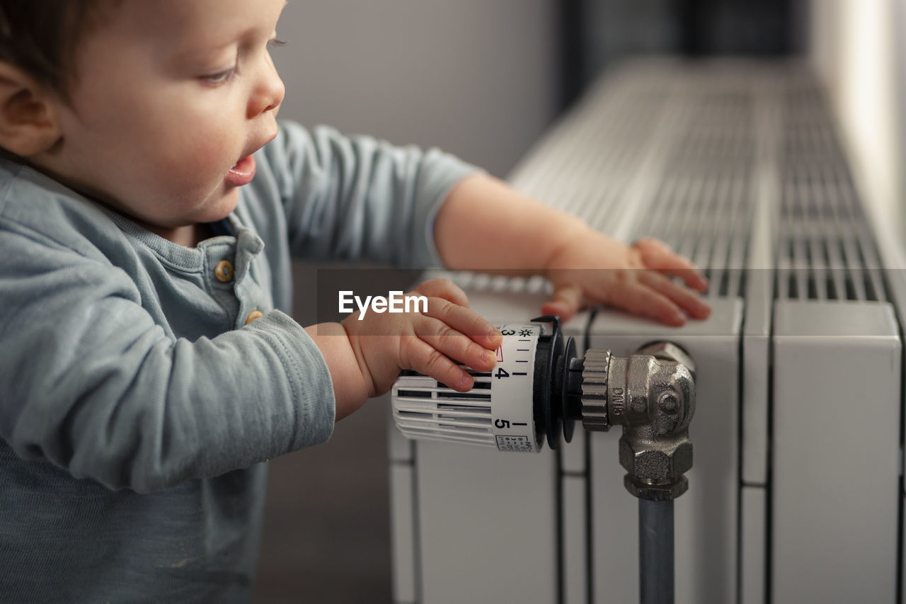 Baby boy playing with thermostat of heater