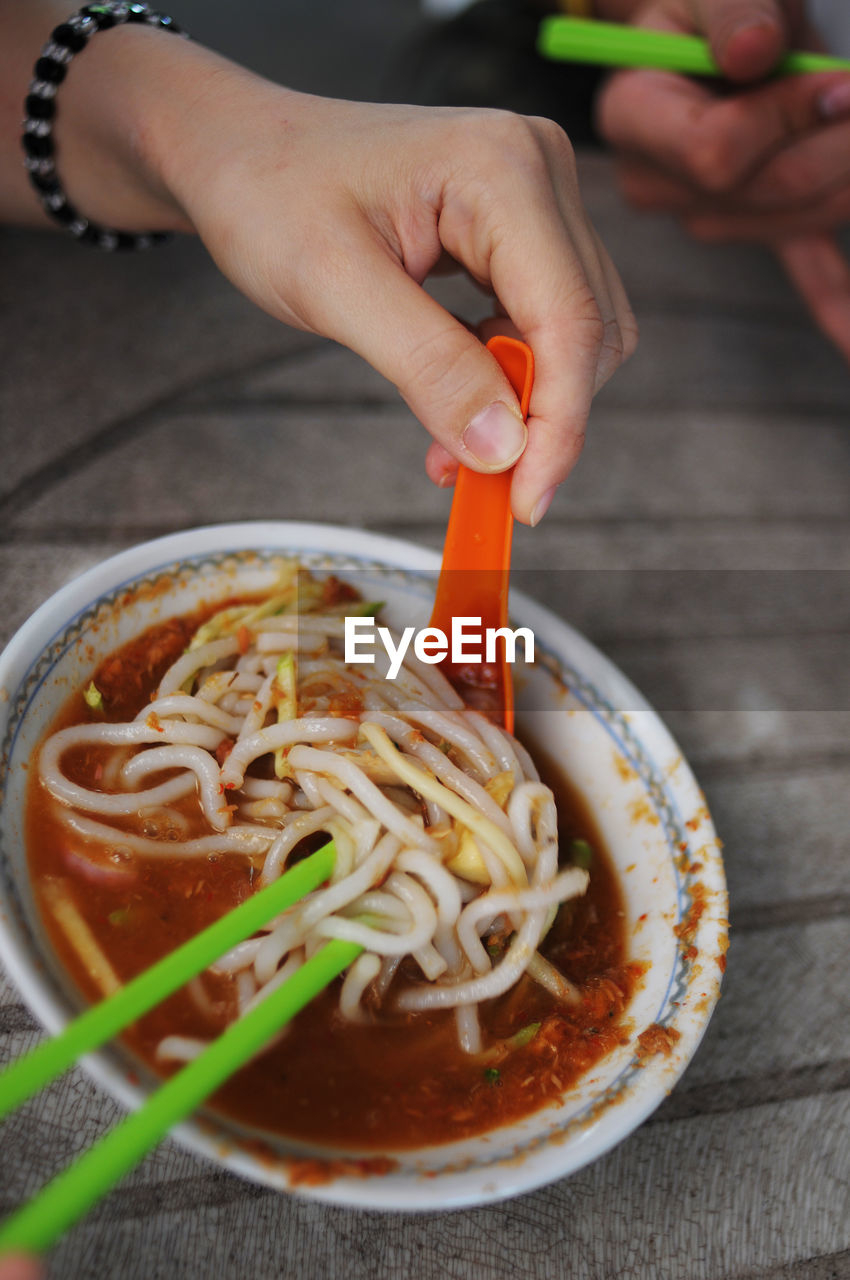 CLOSE-UP OF HAND HOLDING BOWL OF NOODLES