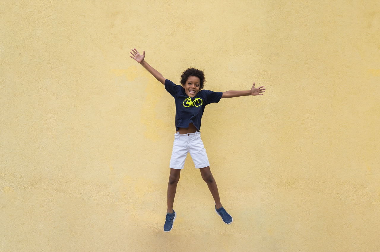 FULL LENGTH PORTRAIT OF HAPPY YOUNG MAN JUMPING IN MOUTH