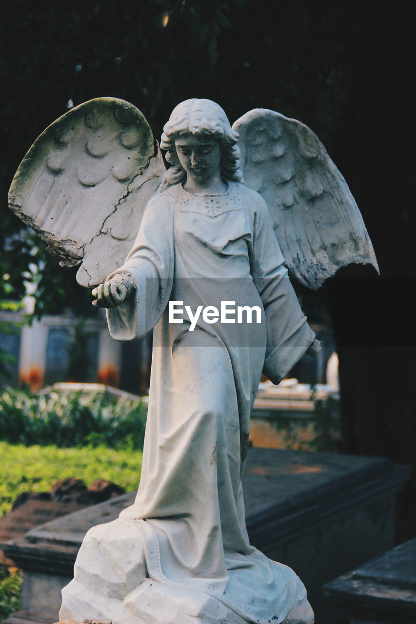 LOW ANGLE VIEW OF ANGEL STATUE AGAINST CEMETERY