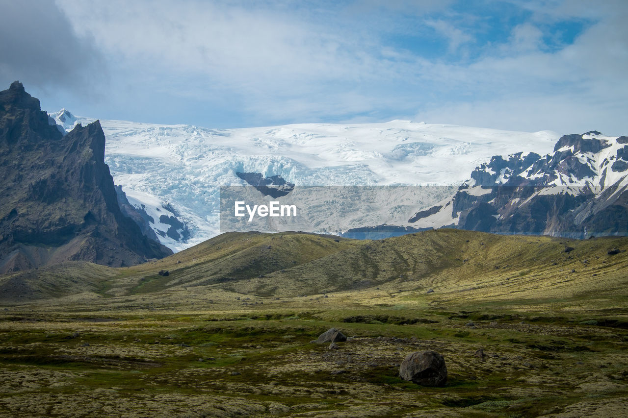 Scenic view of landscape and snowcapped mountains against cloudy sky