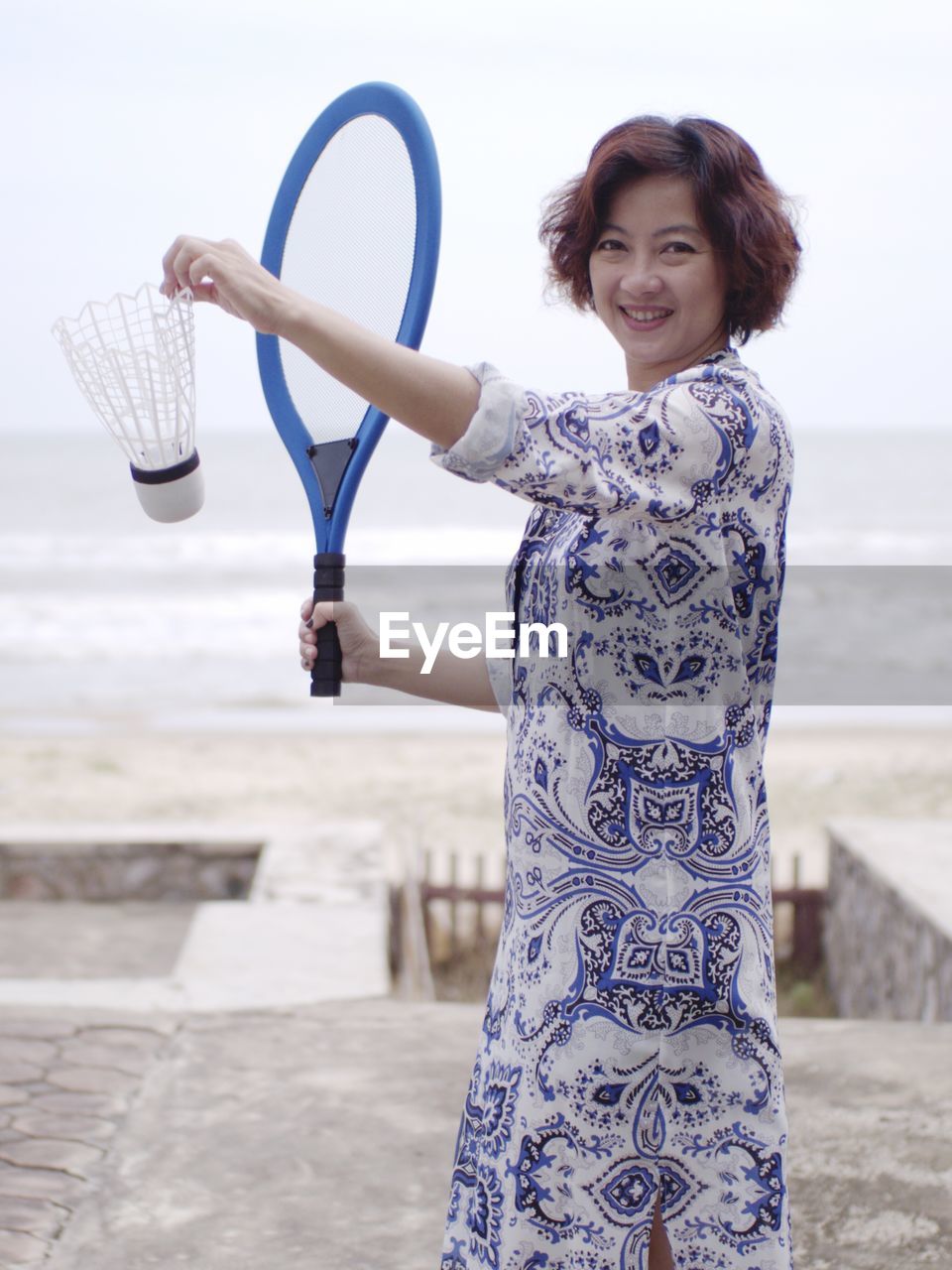 Portrait of smiling woman playing badminton against sea and sky