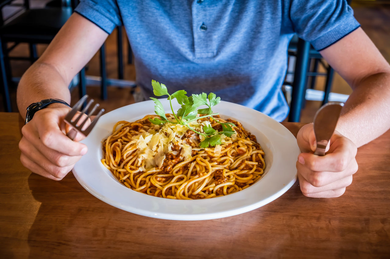 Midsection of man having pasta in plate on table in the restaurant holding utencils