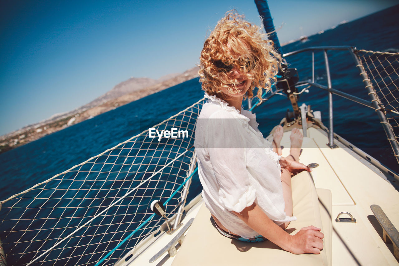 Happy woman with curly hair sitting on boat over sea