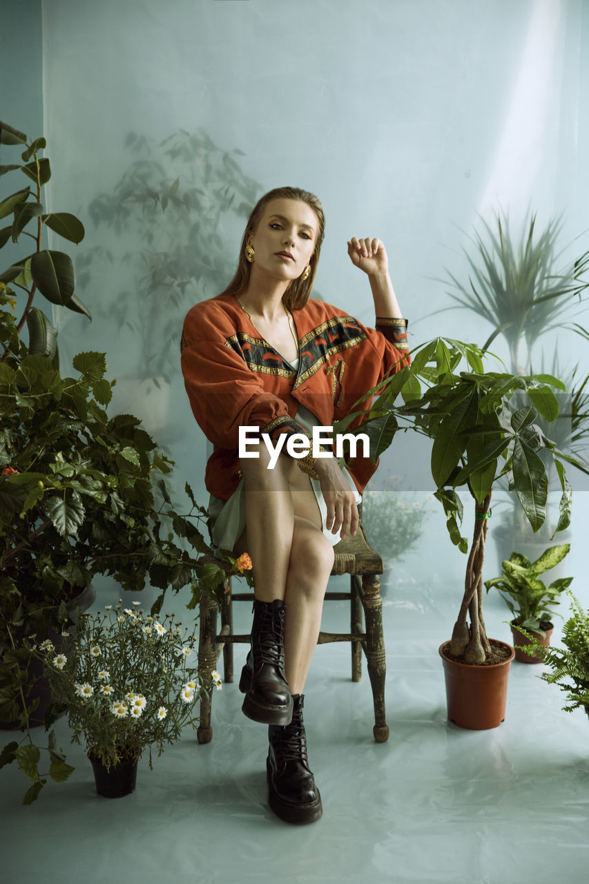 Portrait of young woman sitting on chair against wall