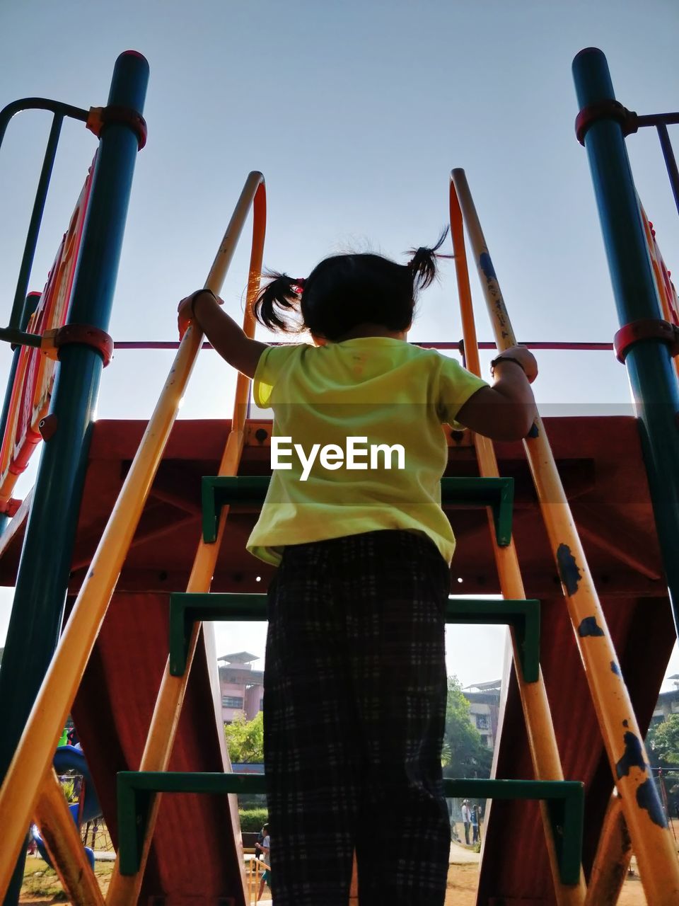 Rear view of girl climbing slide steps in playground against sky