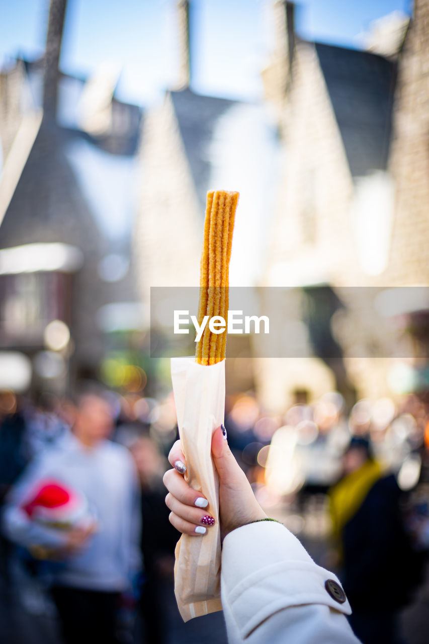 Midsection of woman holding churro in city