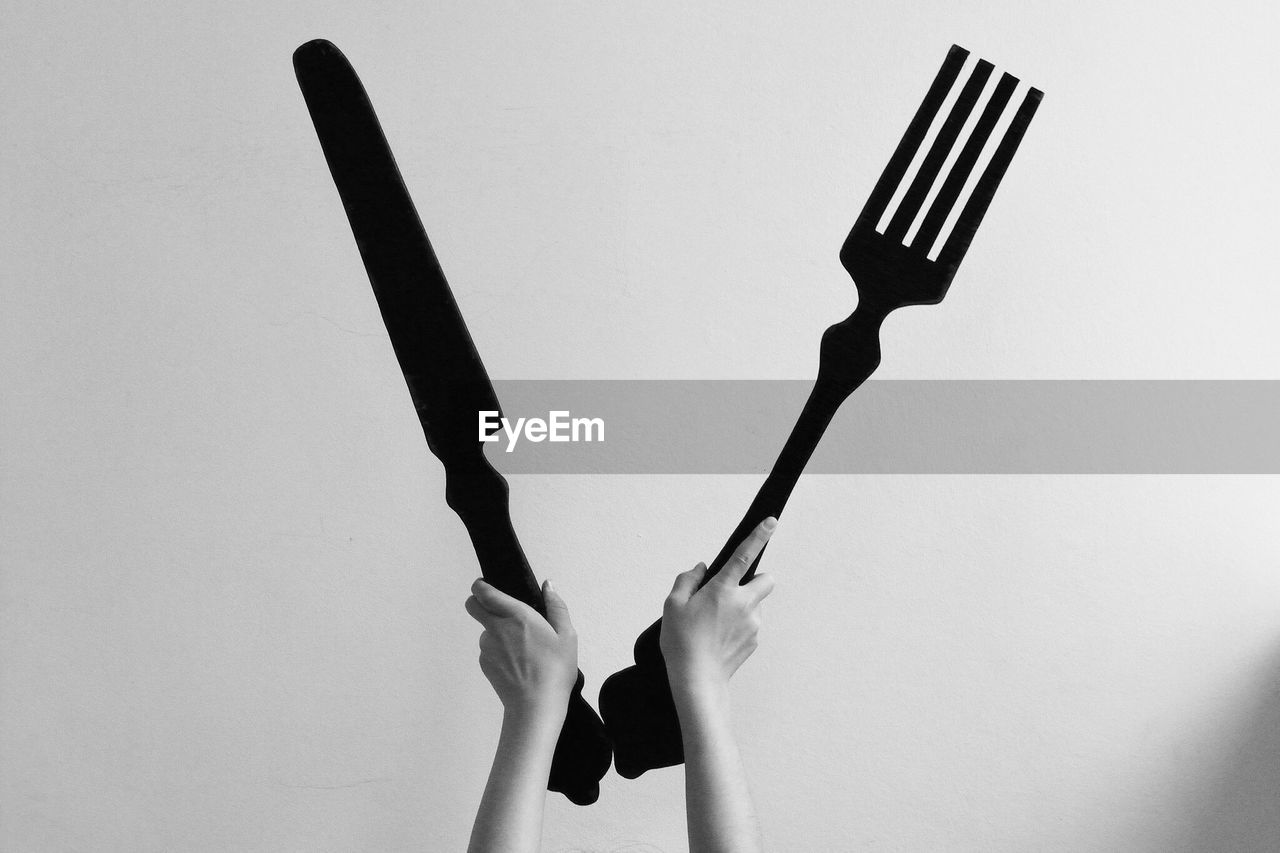 Cropped hands holding large fork and table knife against gray background
