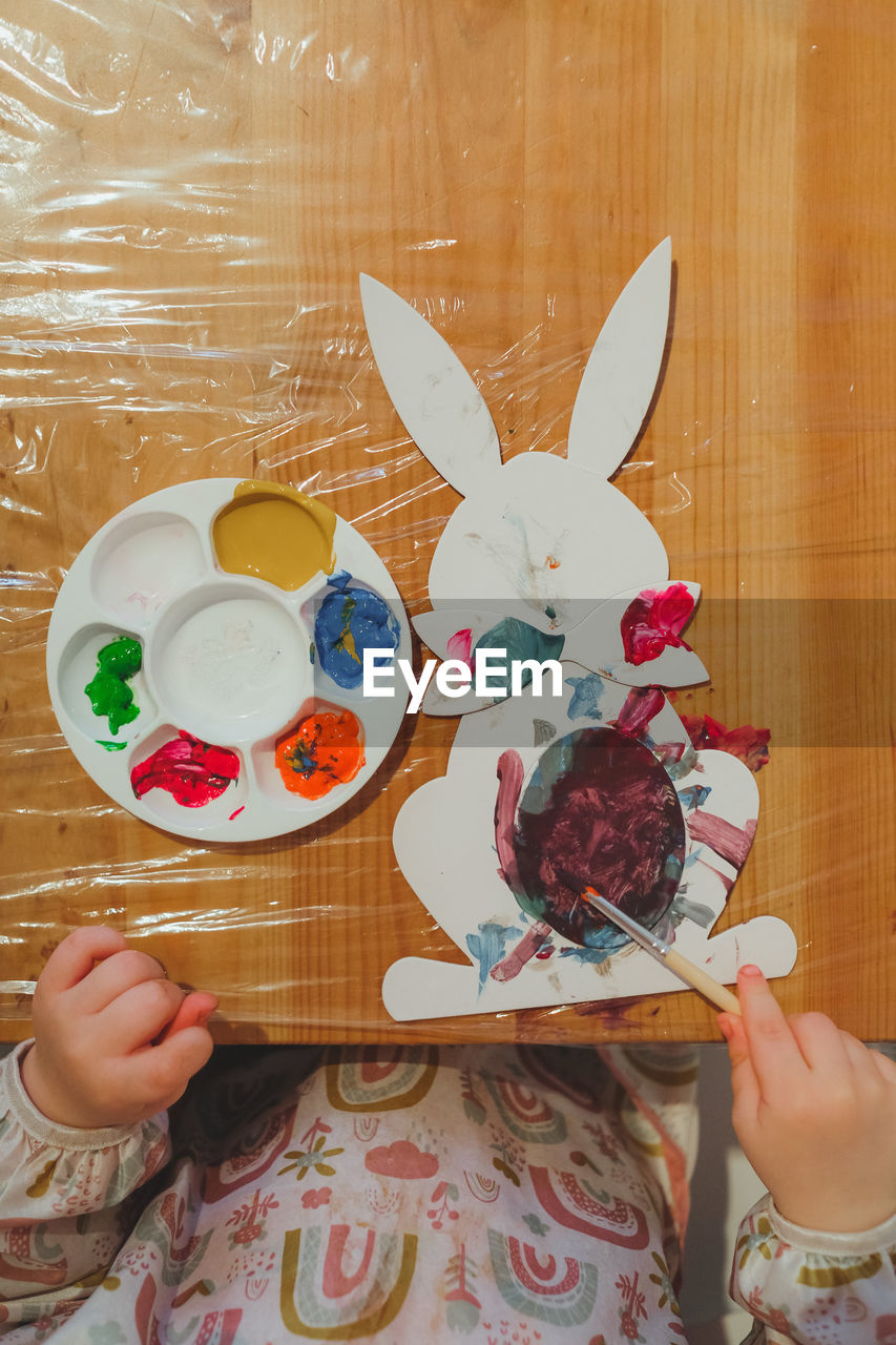 Kid painting easter bunny with paints and brushes