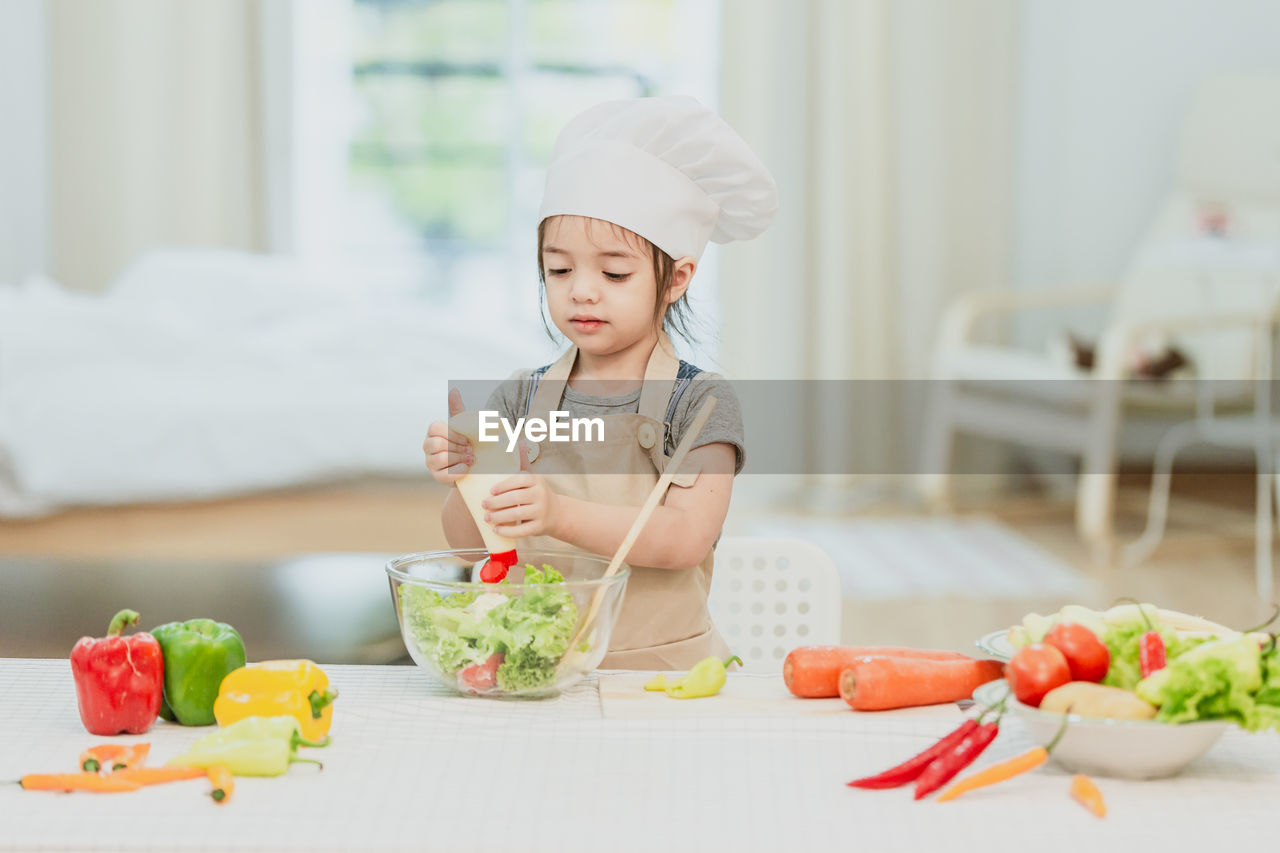 CUTE GIRL PREPARING FOOD ON TABLE AT KITCHEN