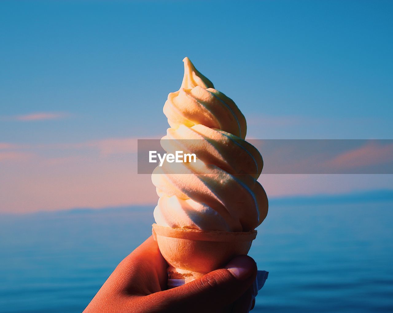 Cropped hand holding ice cream against sea