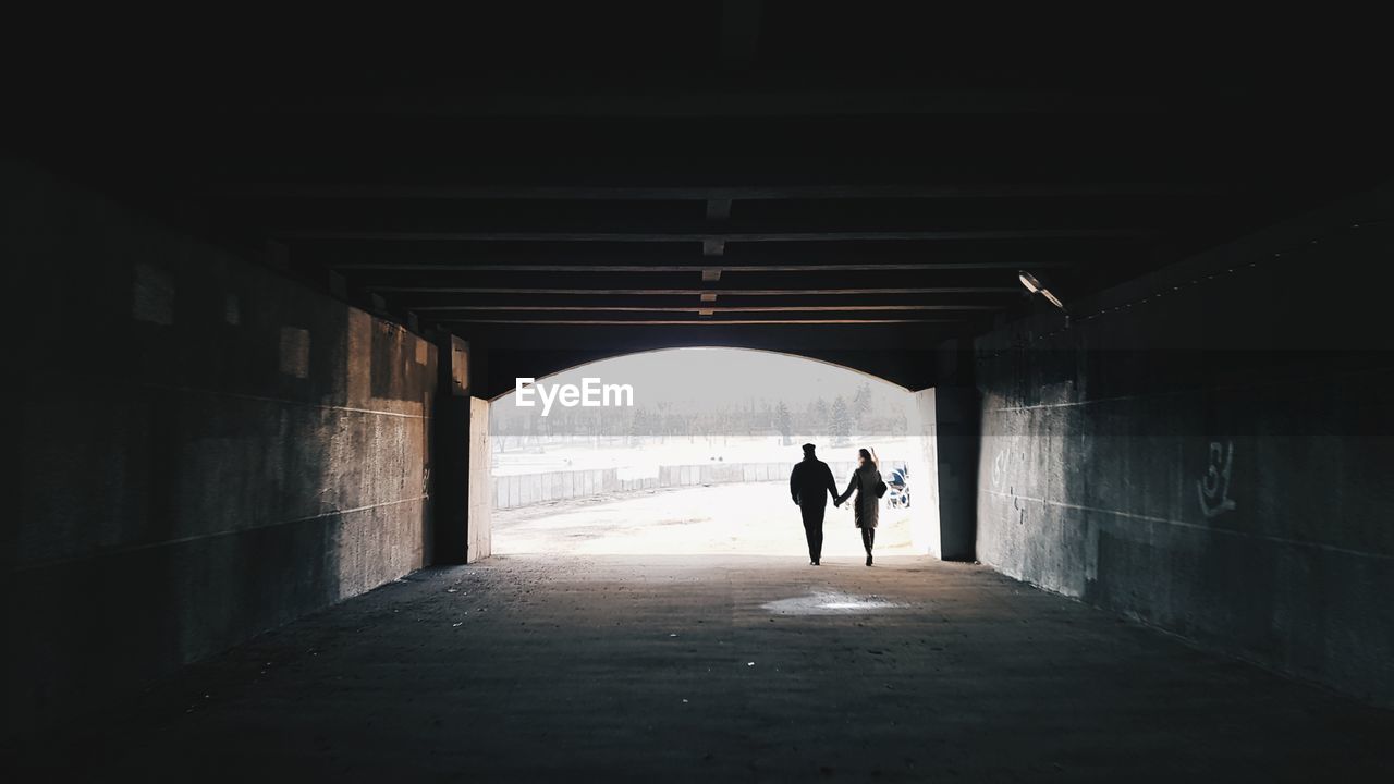 Rear view of silhouette couple walking in tunnel