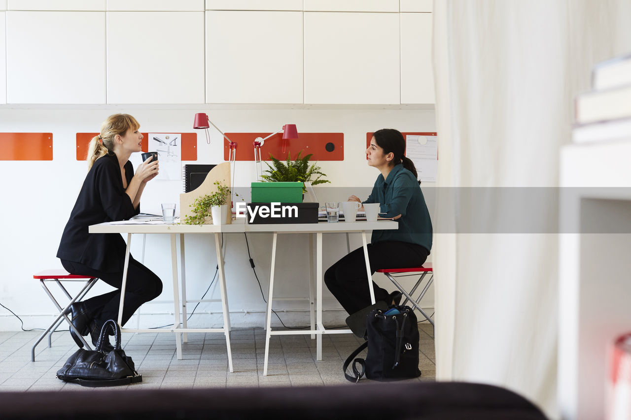Side view of mid adult businesswoman talking at table in office