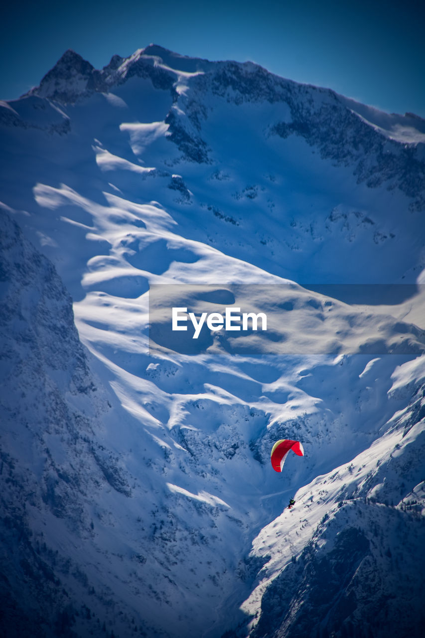 High angle view of person paragliding amidst snowcapped mountain