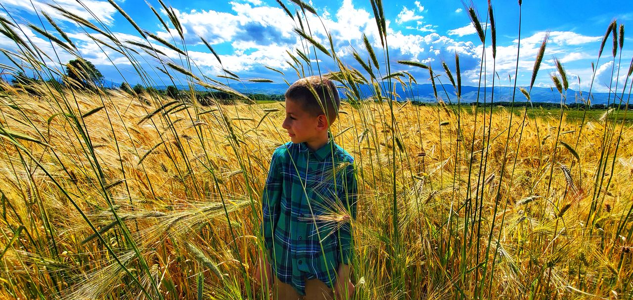 Boy standing on field against sky