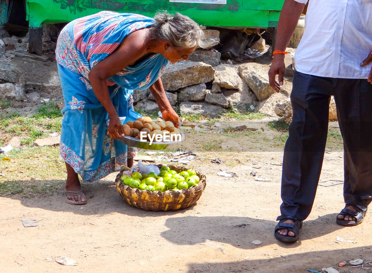 Senior woman bending while standing by basket of fruits for sale
