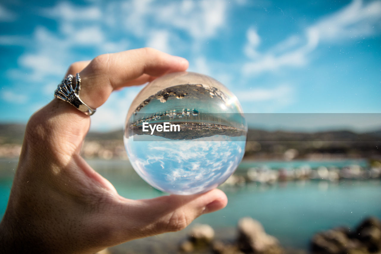Cropped hand of woman holding crystal ball against sky