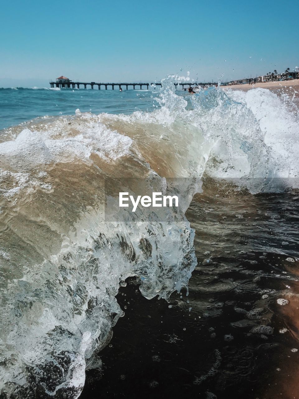Waves splashing at shore against clear sky