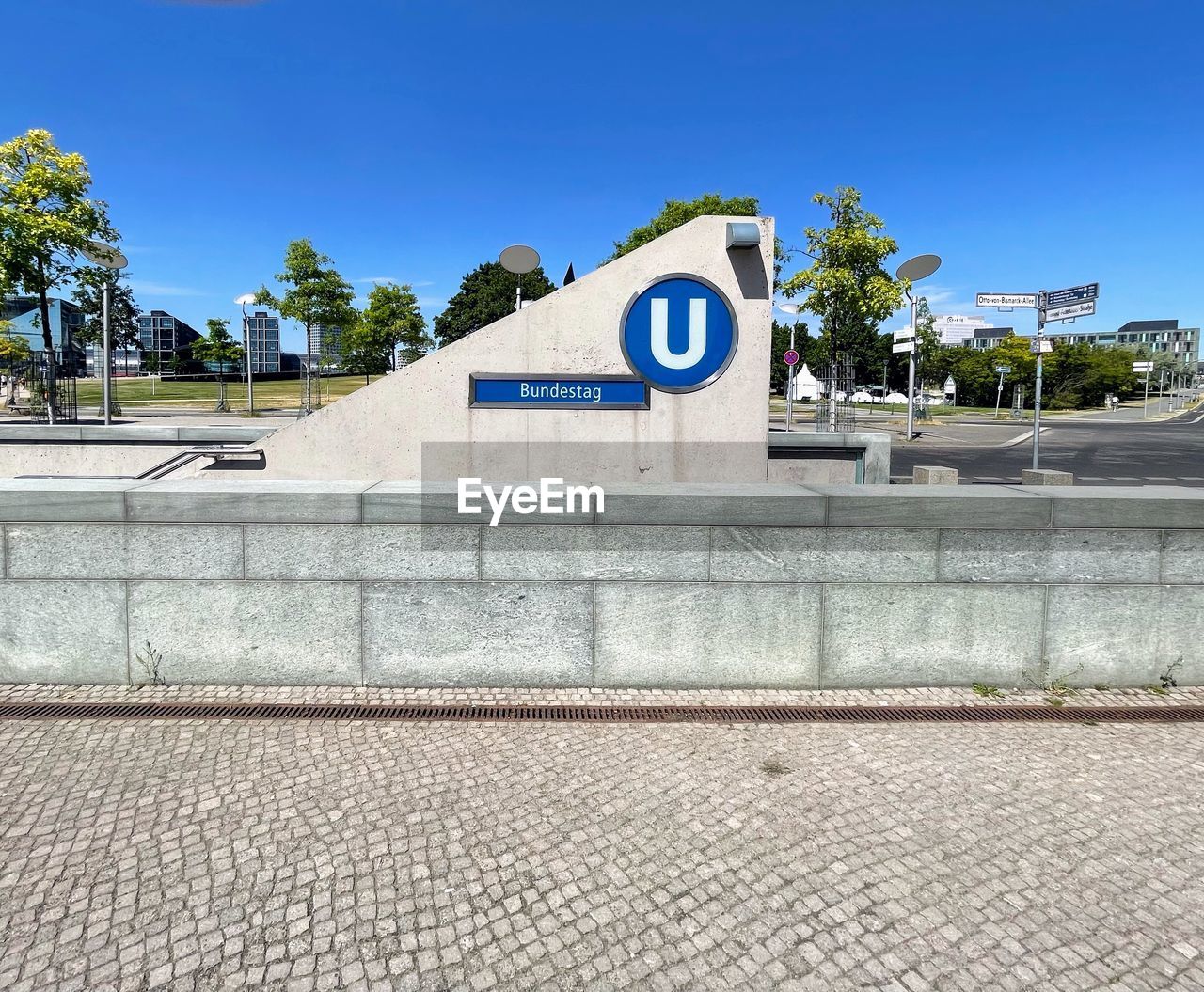 architecture, sign, sky, tree, blue, built structure, communication, plant, nature, wall, no people, city, day, memorial, clear sky, building exterior, road sign, road, text, walkway, street, outdoors, sunny, western script, town square, monument