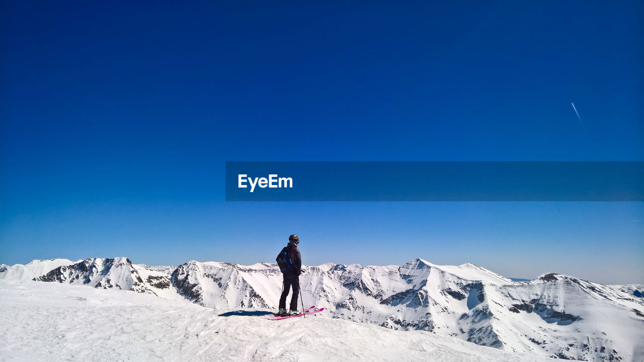 Man standing on snowcapped mountain against clear blue sky