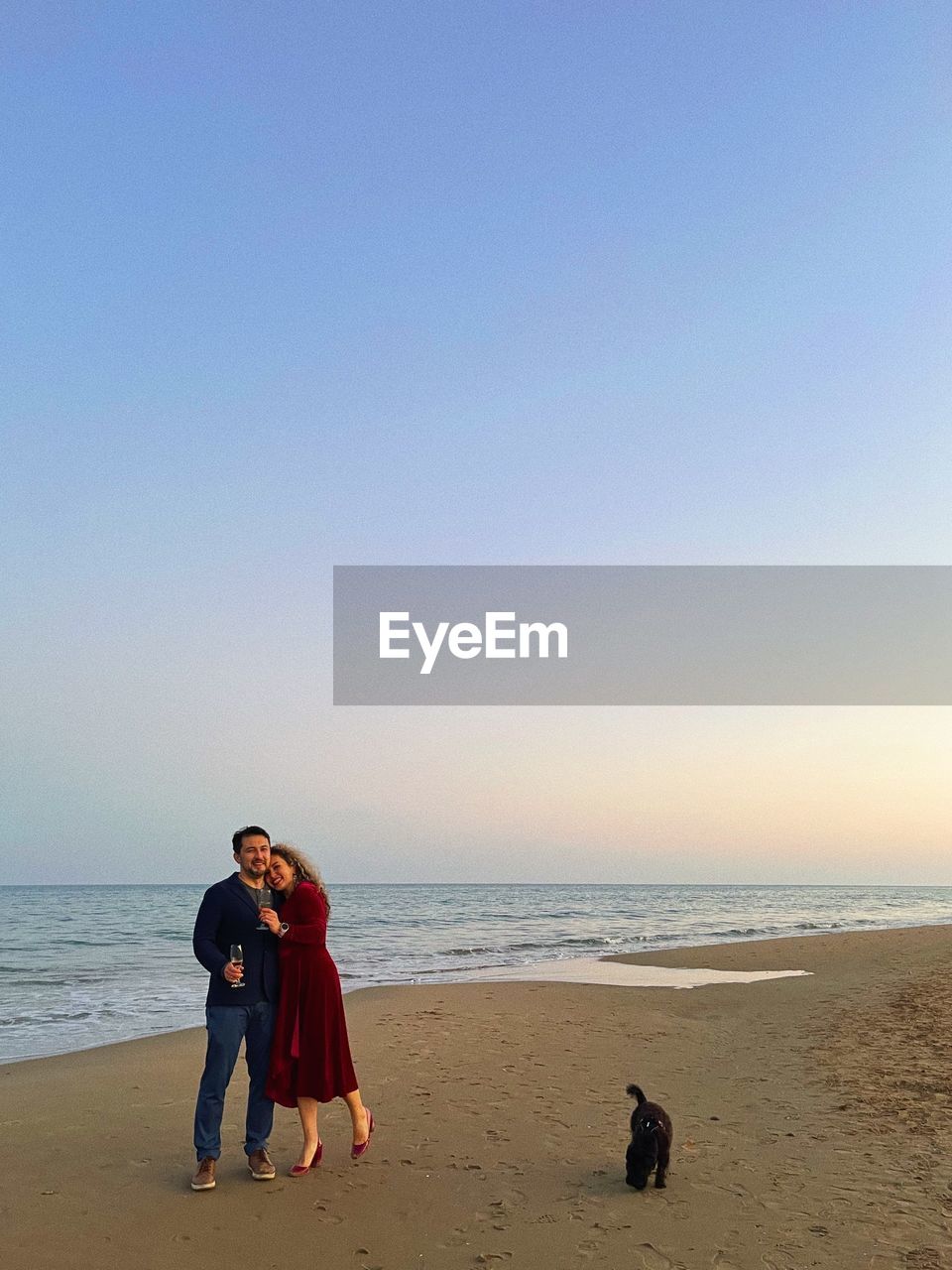 Rear view of woman and man standing at beach against clear sky