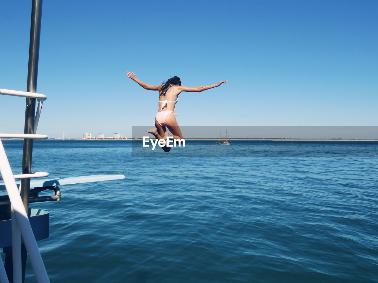 Rear view of young woman jumping in sea against clear sky
