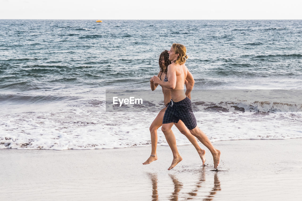 Full length of couple running at beach