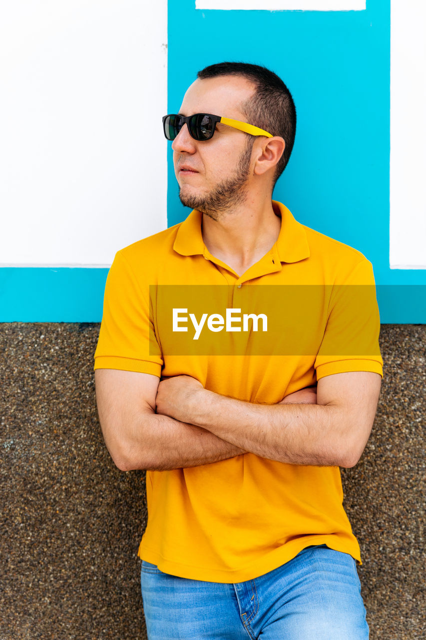 MAN WEARING SUNGLASSES STANDING AGAINST YELLOW WALL