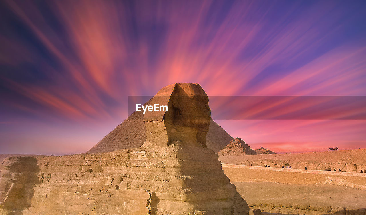 View of great sphinx and pyramid against dramatic sky