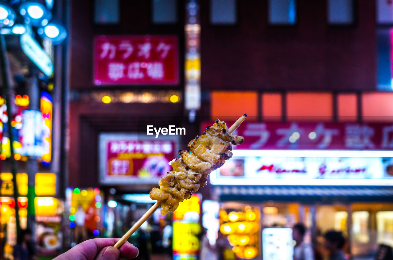 Cropped image of hand holding food on skewer at market