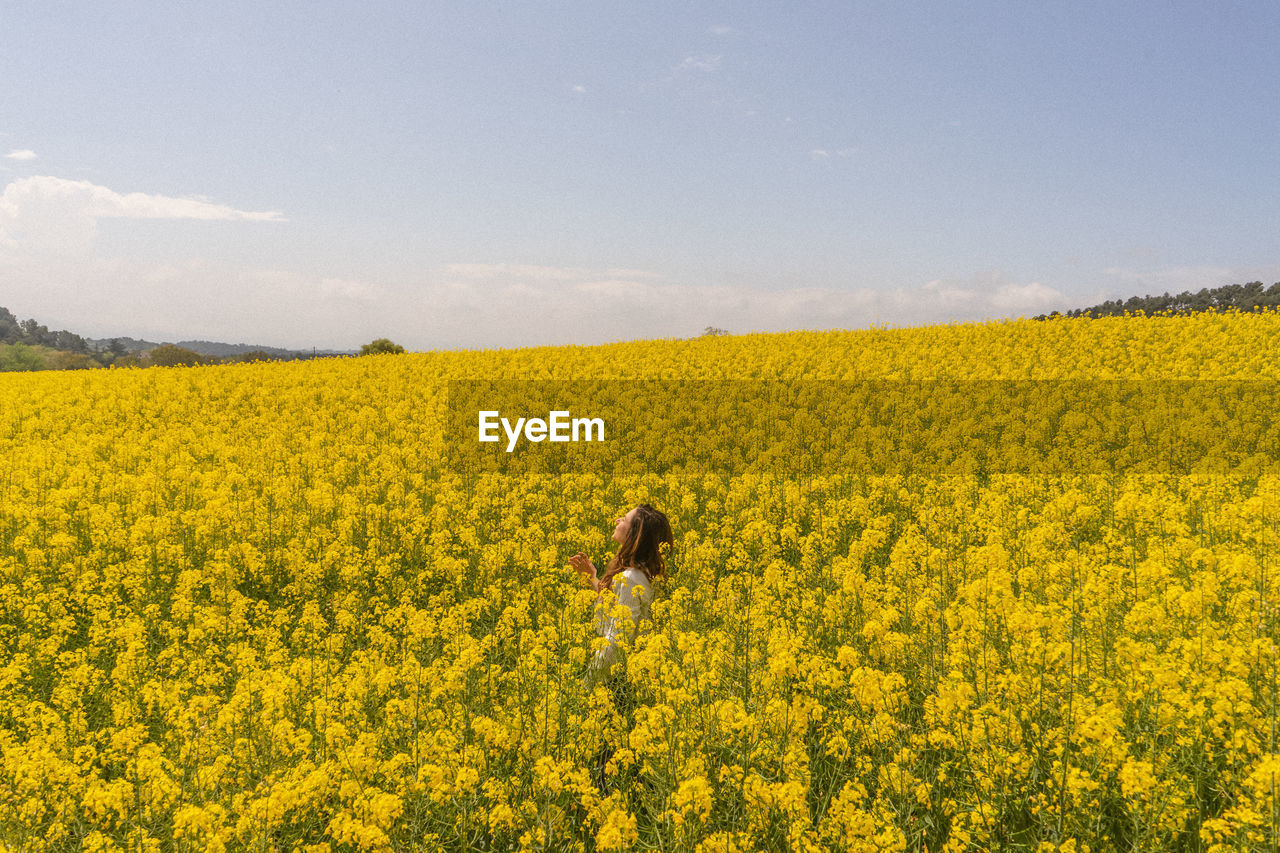 Scenic view of oilseed rape field against sky and a girl in the middle 