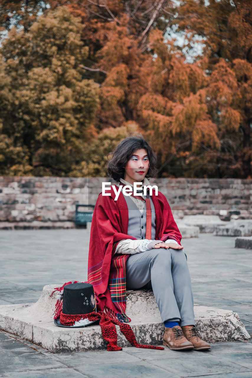 Portrait of young man cosplaying mad hatter sitting in park during winter