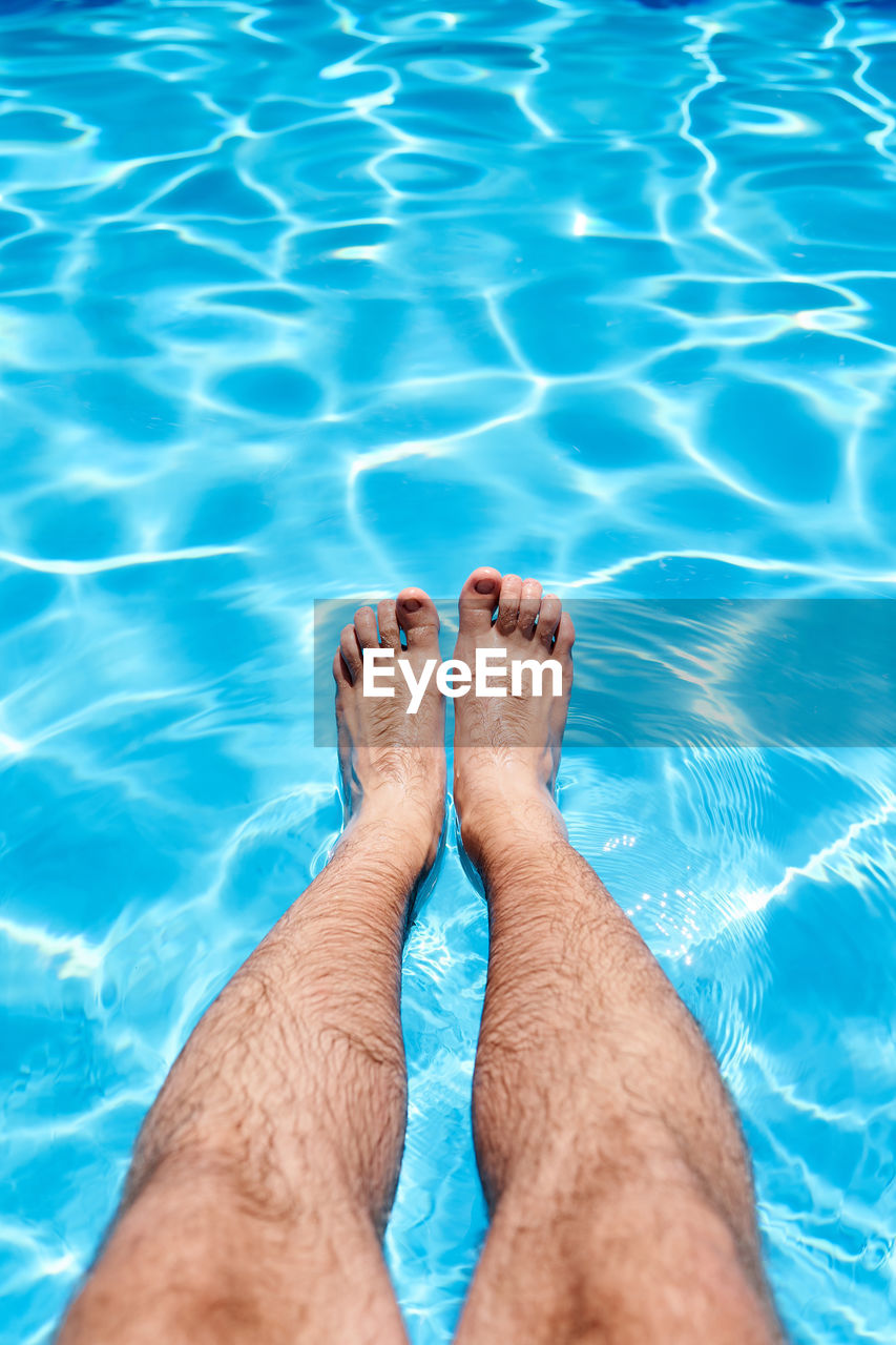 LOW SECTION OF PERSON LEGS AGAINST SWIMMING POOL