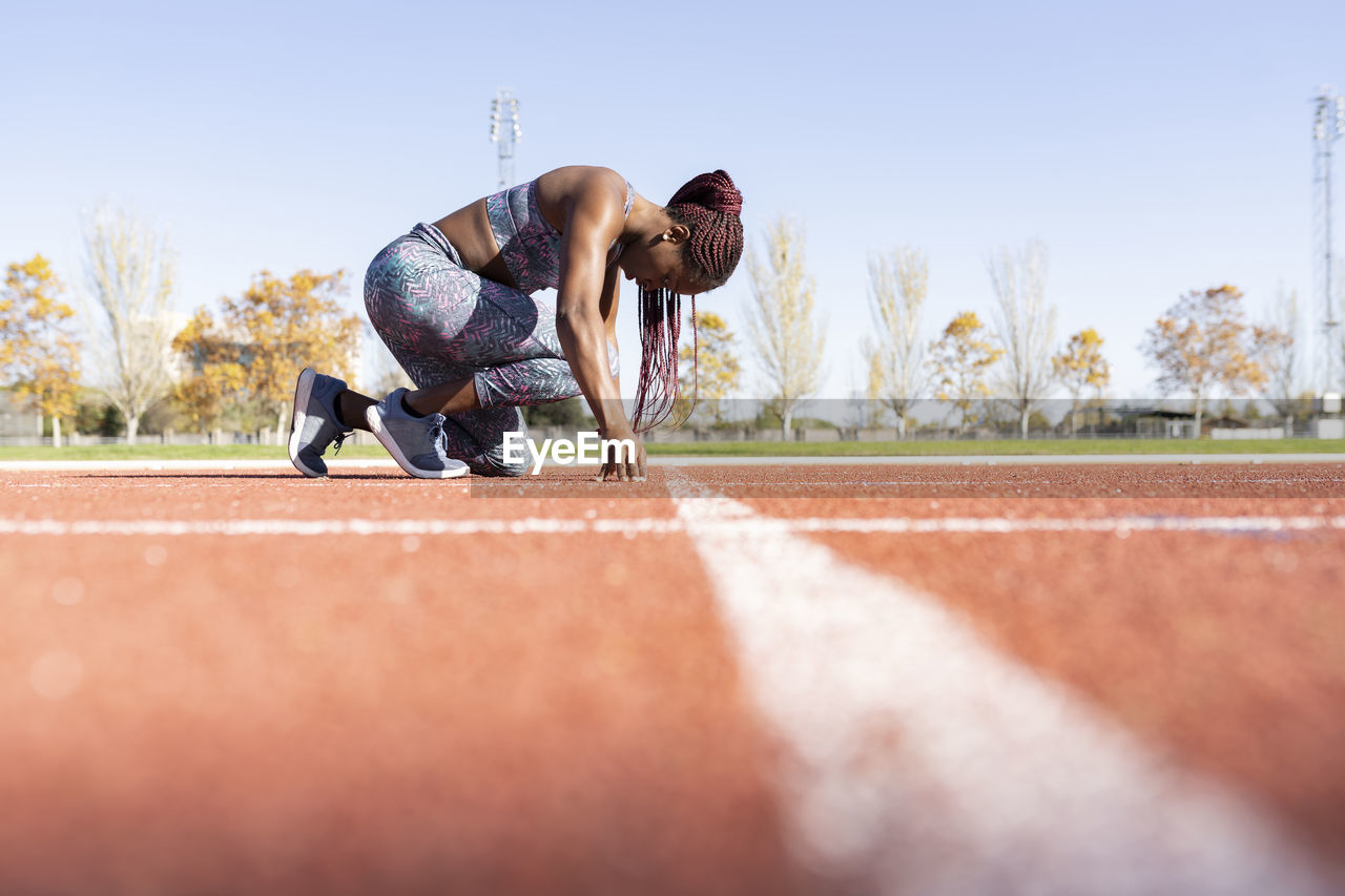 Female athlete in ready position on running track during sunny day