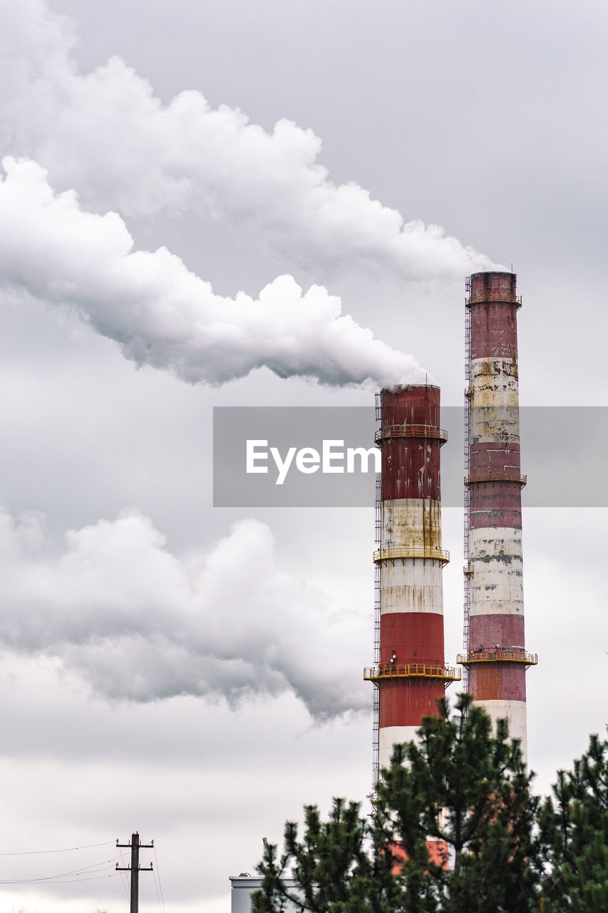 Thick white smoke from industrial factory old rusty chimneys on a cloudy grey sky background,