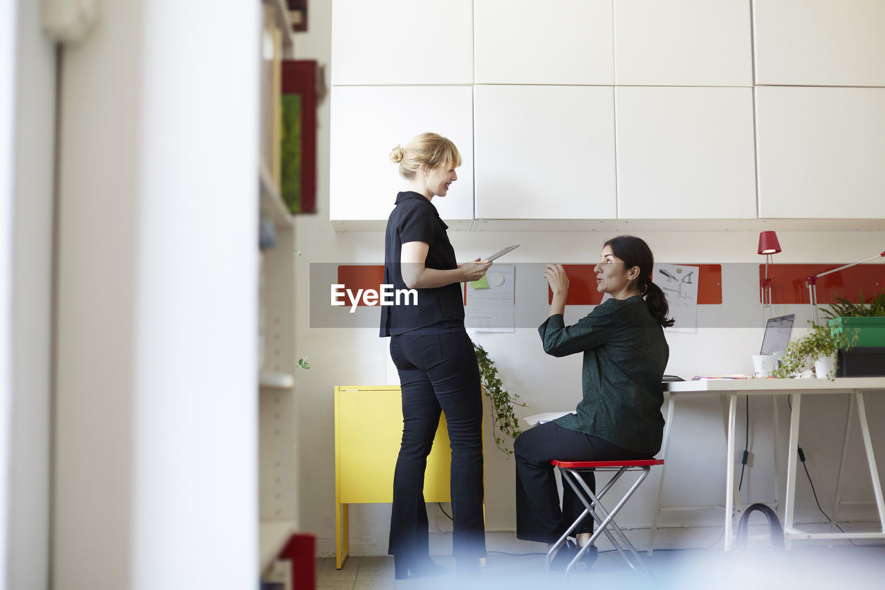 Full length of mid adult businesswoman talking with colleague in office