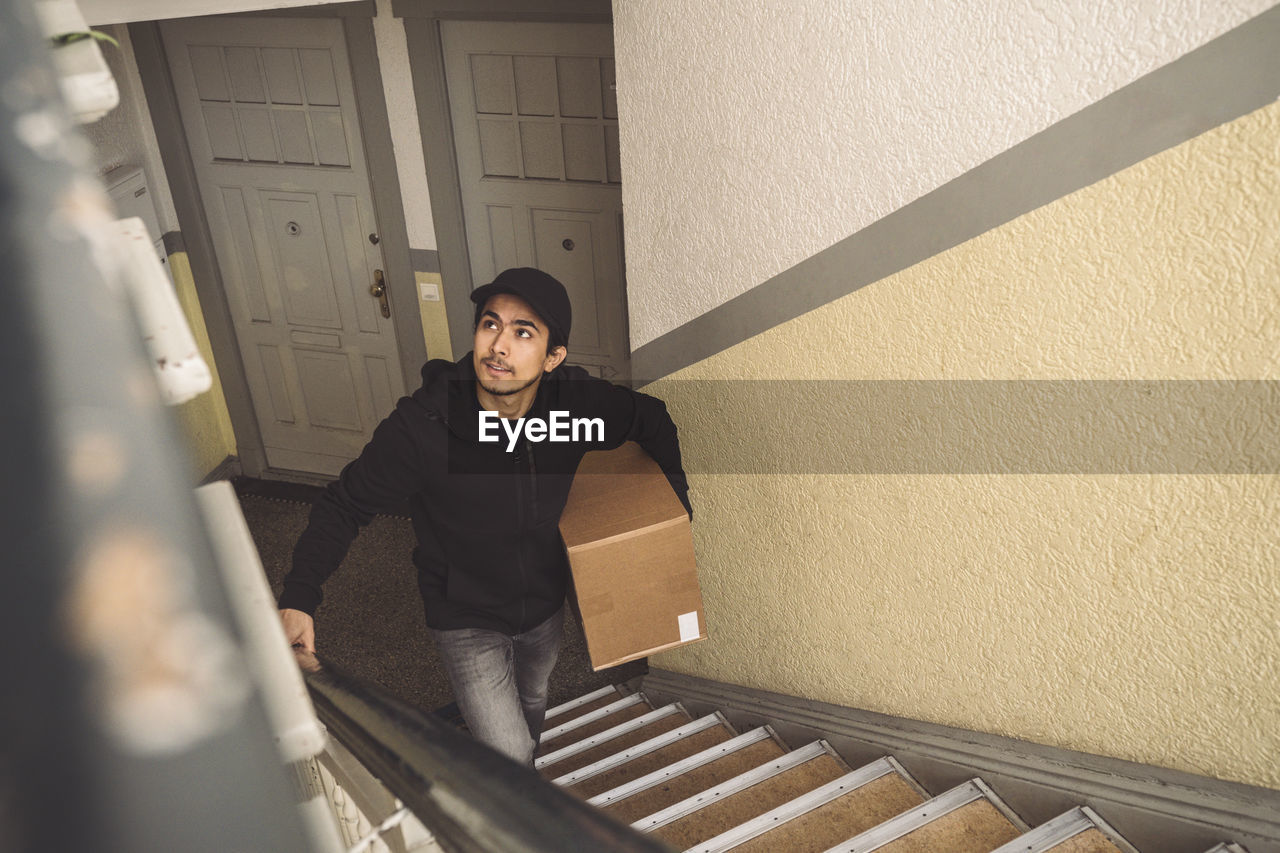 Delivery man with package looking up while walking on staircase