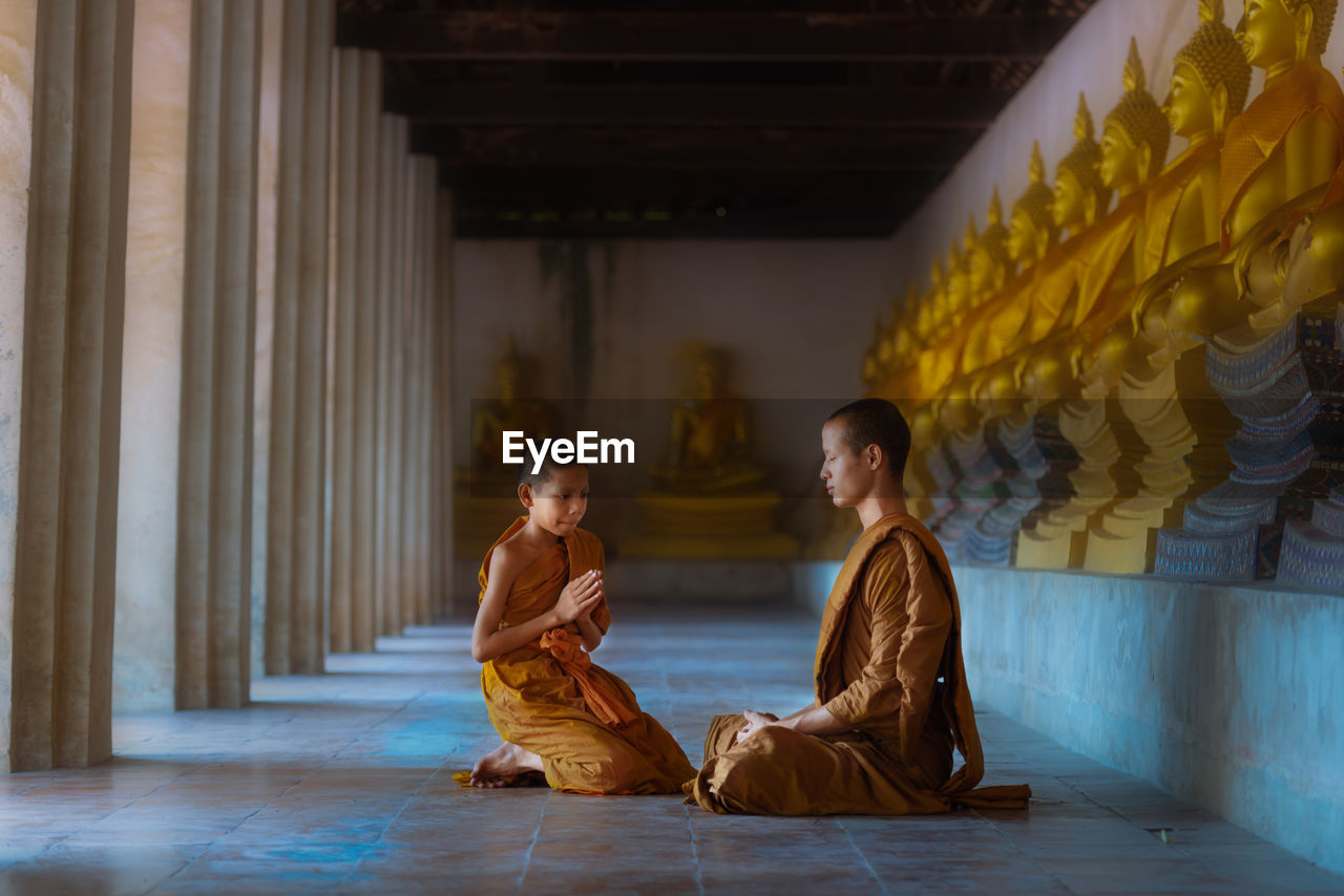 Boy kneeling by monk in buddhist temple