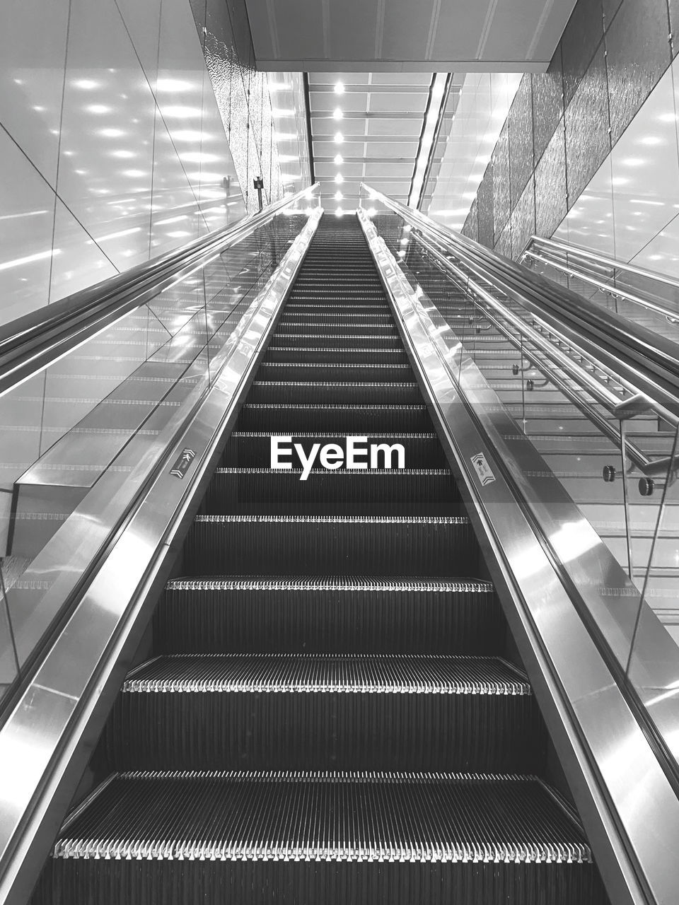 escalator, architecture, convenience, indoors, futuristic, the way forward, staircase, built structure, steps and staircases, moving walkway, transportation, technology, railing, line, illuminated, no people, low angle view, monochrome, black and white, diminishing perspective, pattern, metal, city, subway station, travel, ceiling