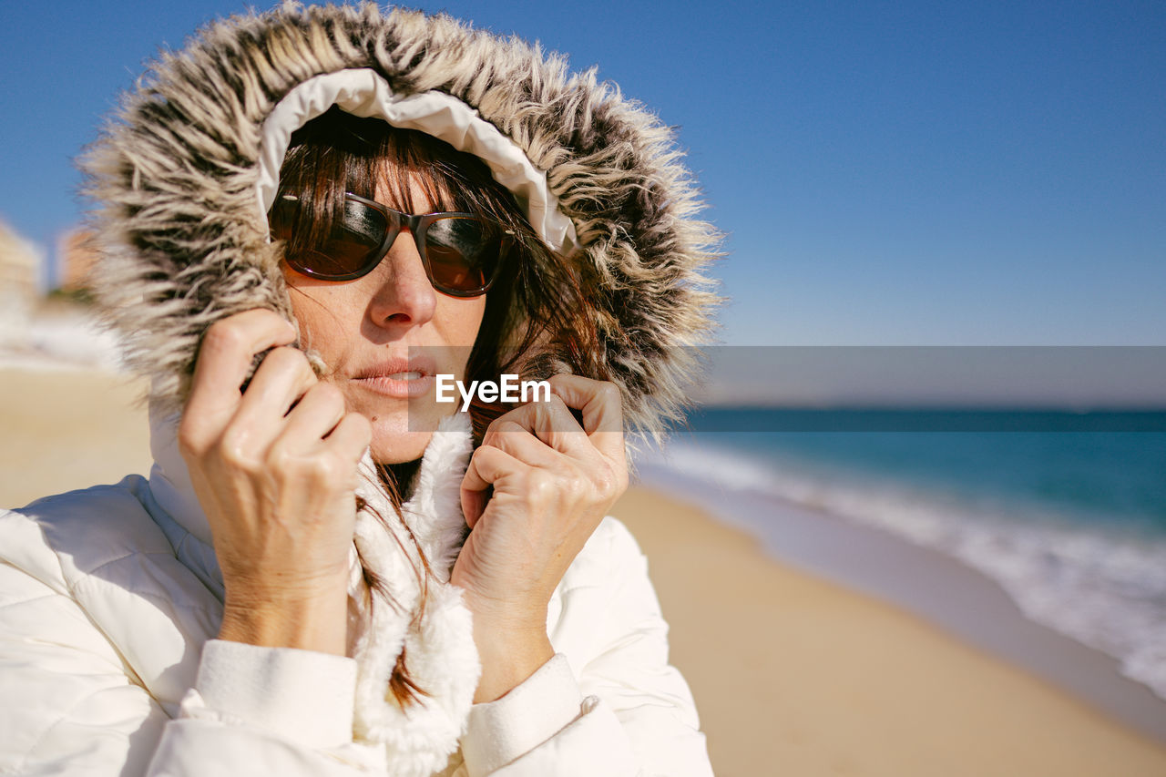 Beatiful mature woman in white jacket and sunglasses on a sunny winter day at the beach