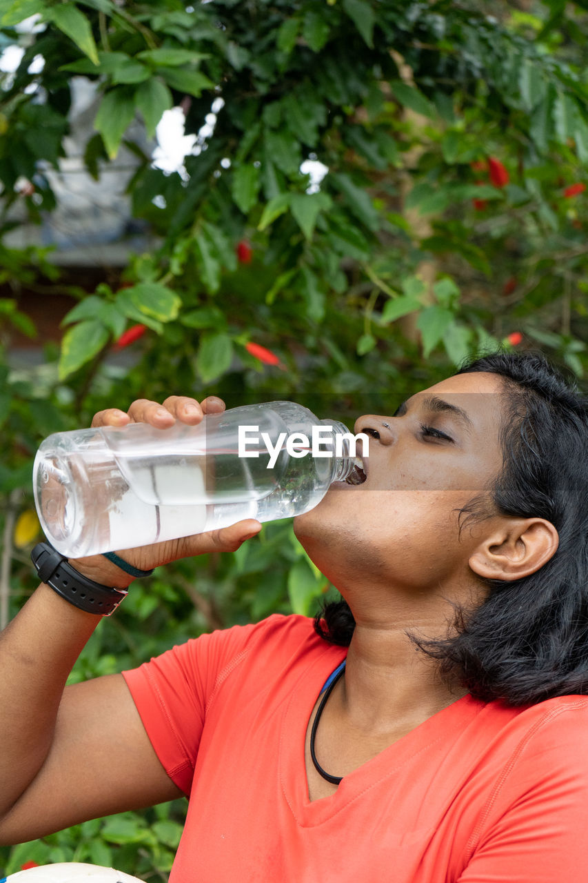Woman drinking water from bottle against plant