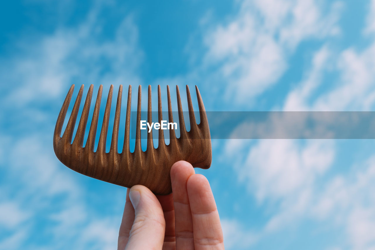 Close-up of hand holding comb against sky