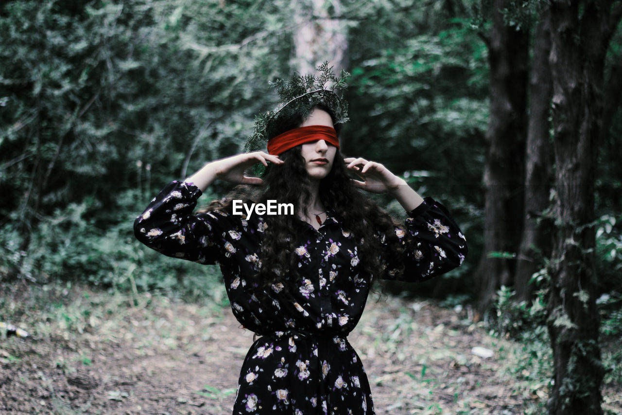 Fashionable young woman with blind fold while standing in forest