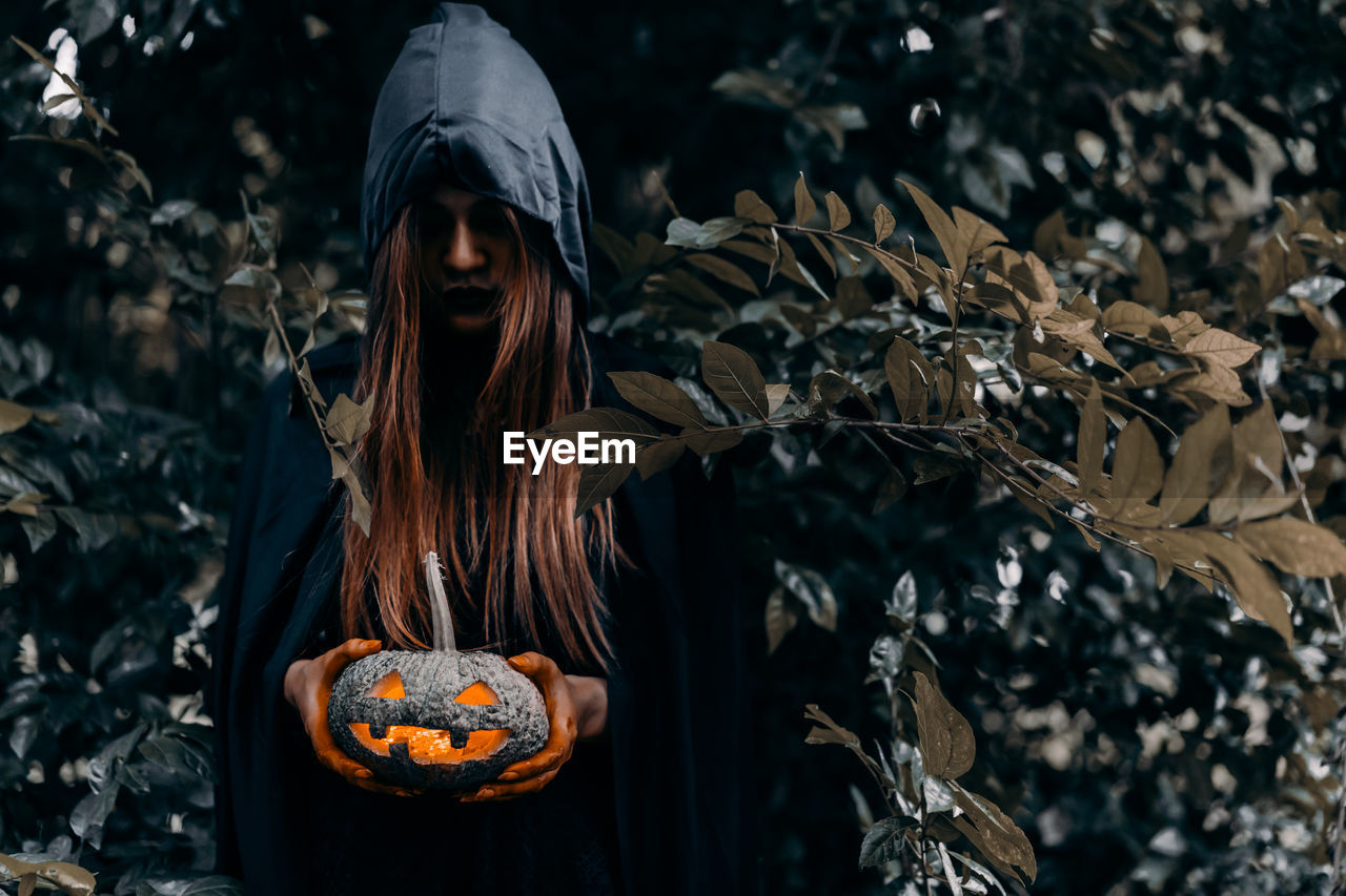 Young woman holding jack o lantern at forest during halloween 