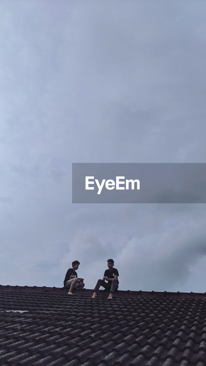 Low angle view of men on roof against sky