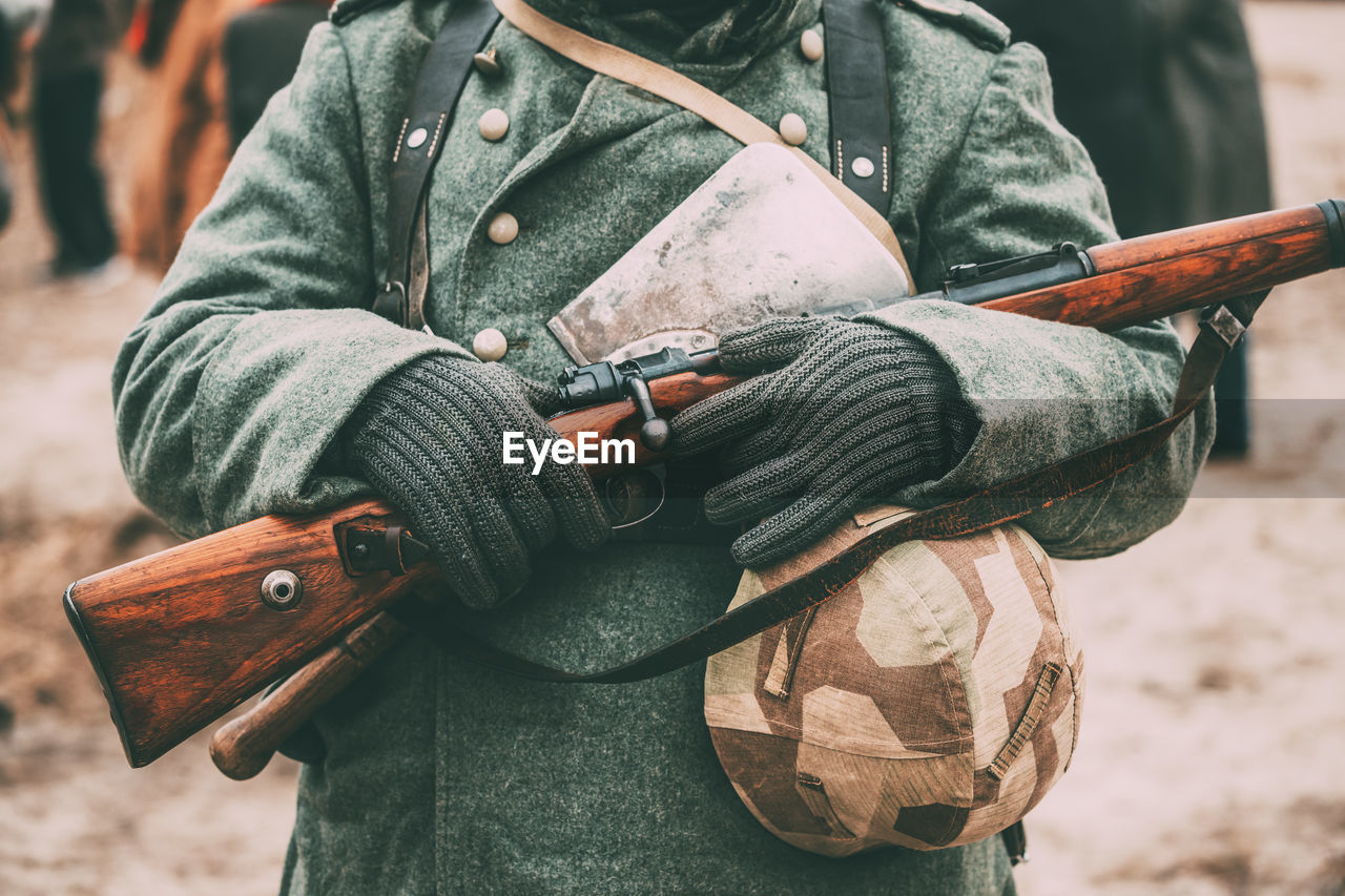 Midsection of soldier holding gun and hat