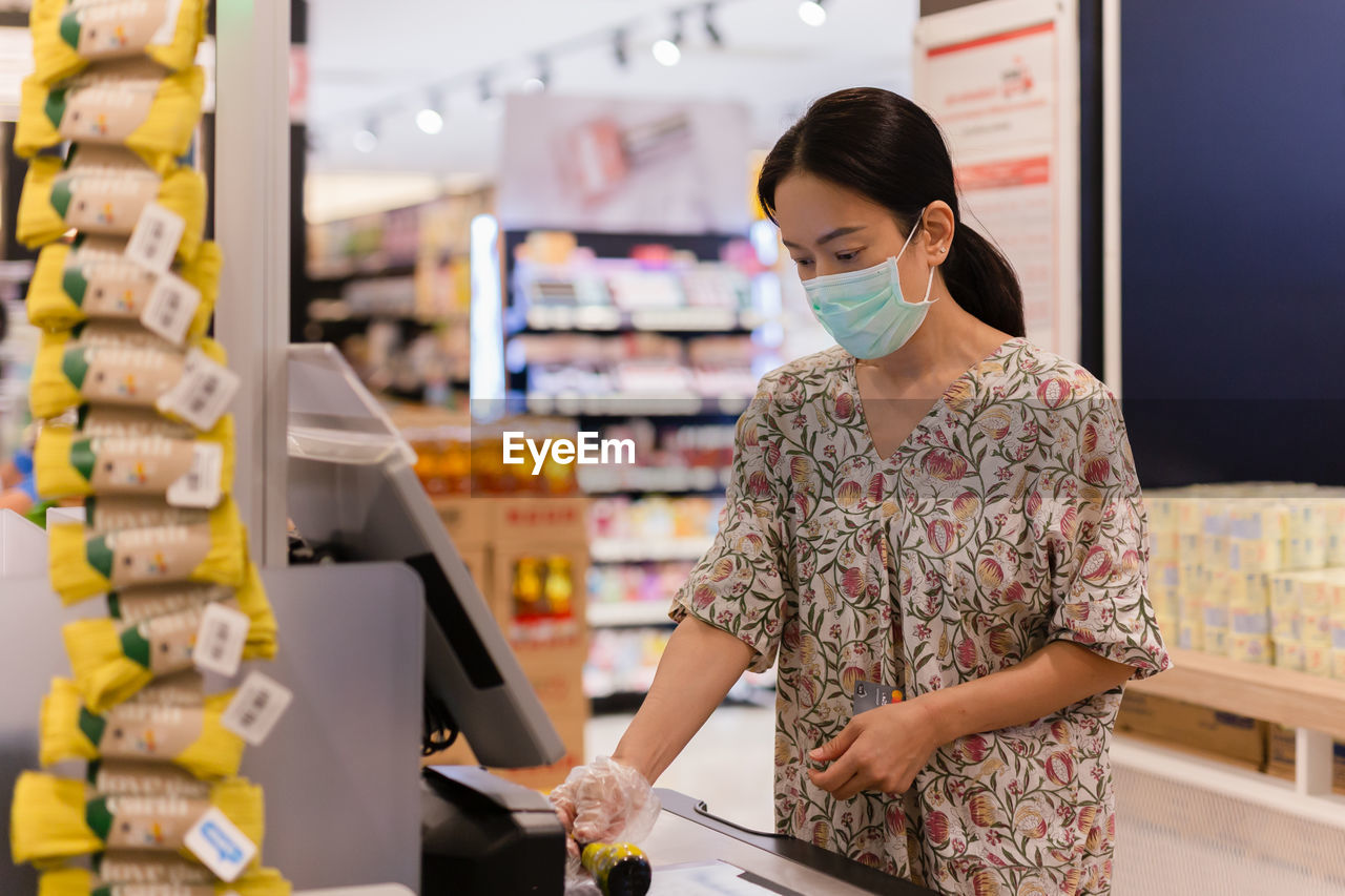 Woman customer in protective mask self service check out till and digital bar code scanner.