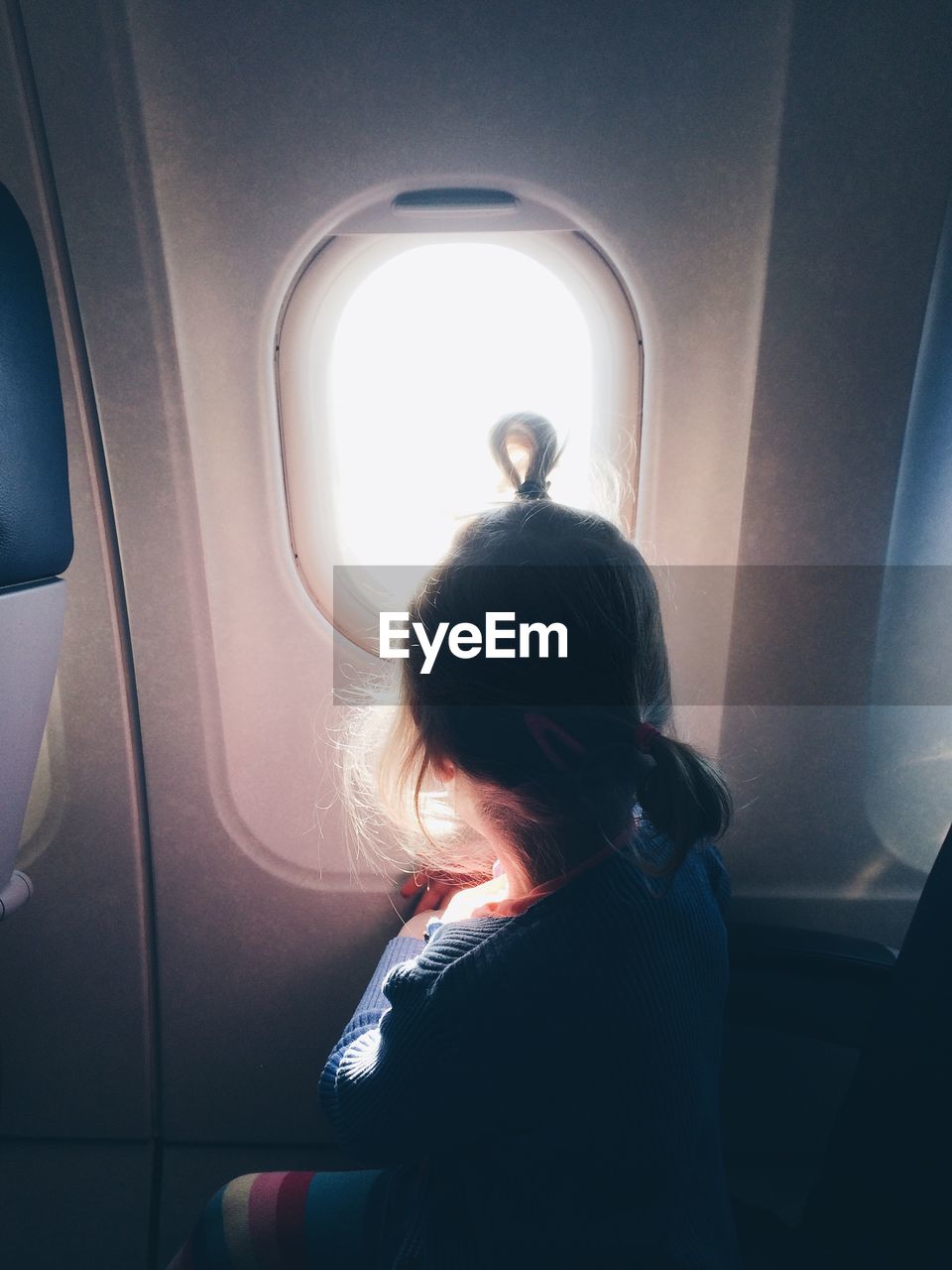 Side view of girl looking through window in airplane