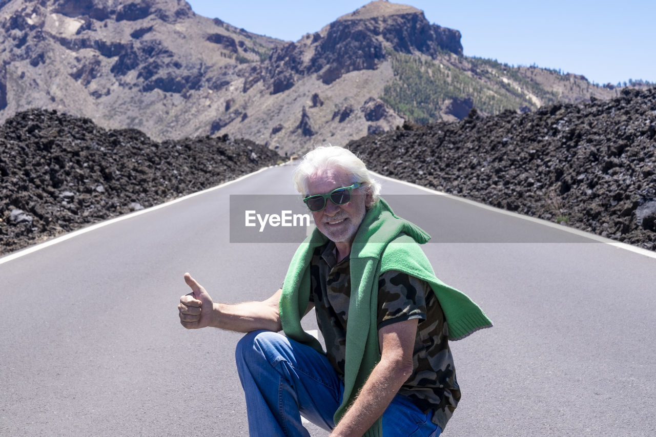 Portrait of smiling man gesturing while crouching on road